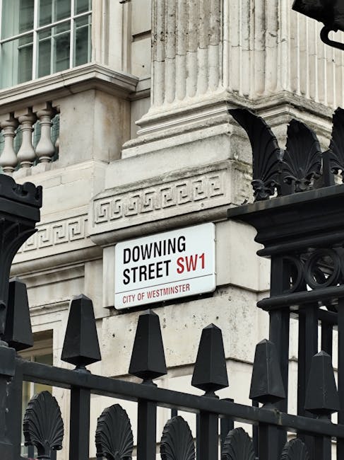 A street scene in Pimlico showing a London Underground sign for Westminster Station hanging above a black signboard that indicates public subway, toilets, and staff, with an image of a red double-decker bus partly visible below. In the background, there is a historic building with ornate architectural details, large windows, and decorative columns, along with a flag flying atop the structure. On the pavement and near the building, trees with green foliage are visible, and a streetlamp stands to the right. The scene is captured during daylight with partly cloudy skies, reflecting typical urban surroundings in Westminster. The context relates to house removals and the logistics of moving within or around Westminster, with natural lighting and an emphasis on street infrastructure supporting relocation activities, as seen through the signage and urban environment.